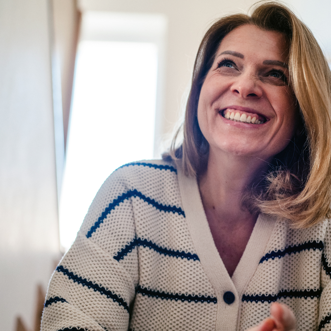 A woman in her mid-forties laughing in a sunlit kitchen